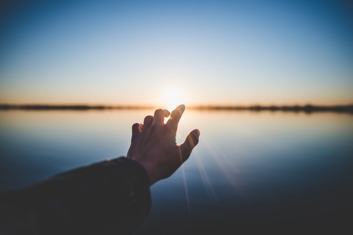 Hand reaching toward light on the horizon — representing the clarity of knowing and presenting your strengths
