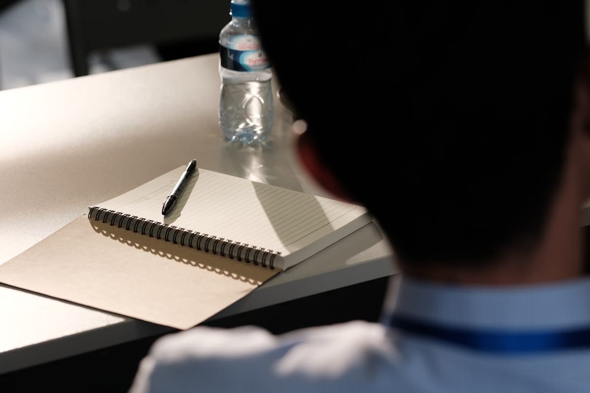 A focused candidate at a desk with an open notebook and pen, mid-preparation: the individual prep work the article describes