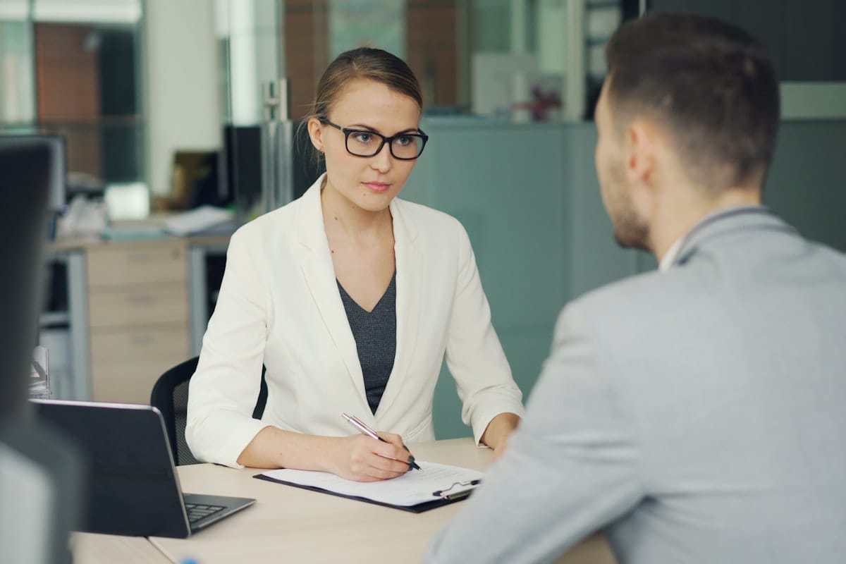 A candidate facing an interviewer across a desk in a modern office, mid-interview