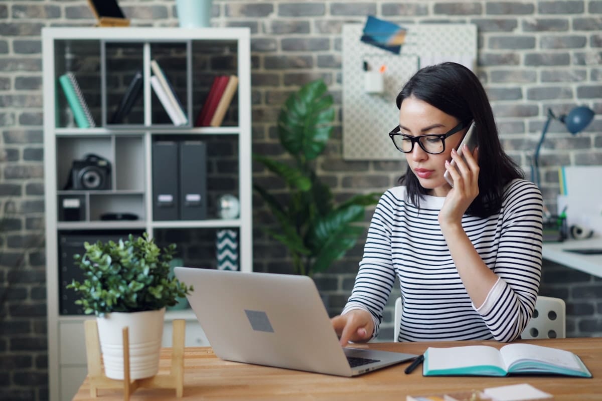 A focused candidate at a home-office desk with a laptop and an open notebook, taking a call while preparing