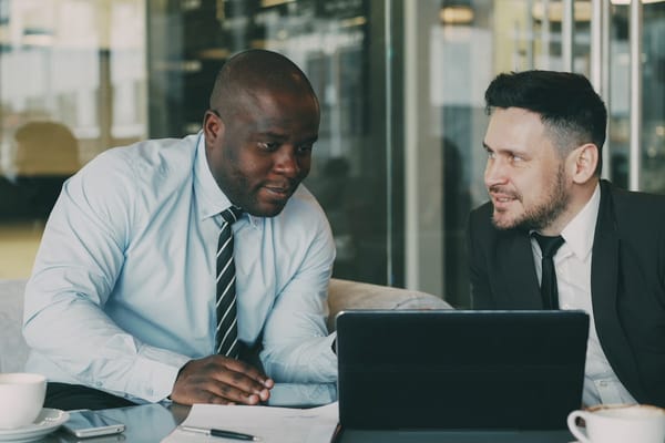 Two consulting professionals discussing over a laptop in a glass-walled office