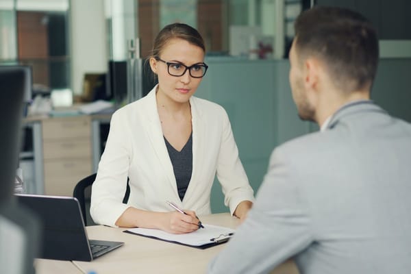 A candidate facing an interviewer across a desk in a modern office, mid-interview
